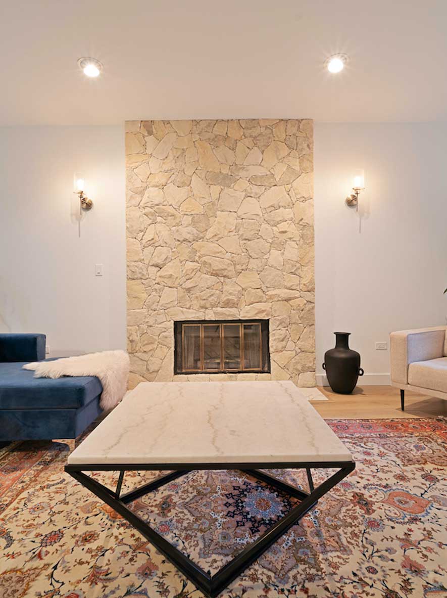 Living room with recessed pot lighting and matching wall sconces flanking a stone fireplace