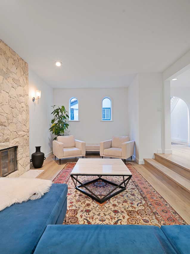 Living room with recessed pot lighting and a wall sconce beside a stone fireplace